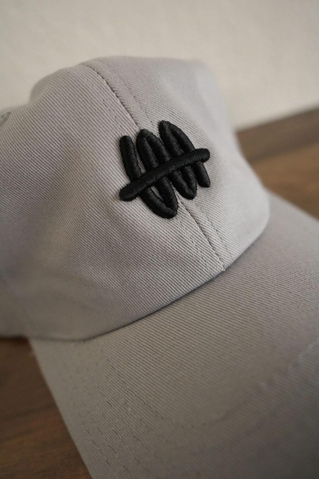 Close-up of a gray cap with a black logo on a neutral background